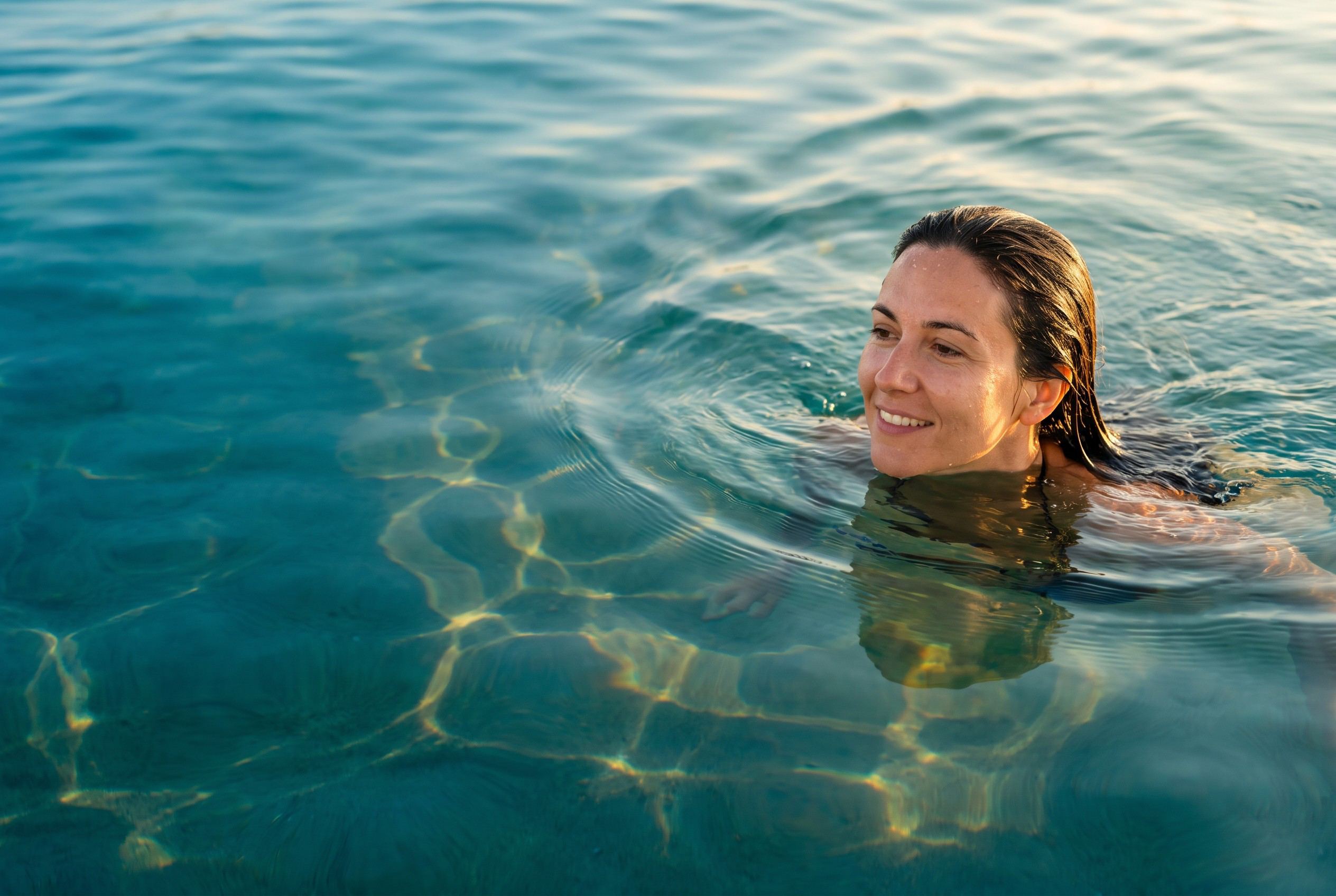 Eine Frau taucht lächelnd aus klarem, türkisem Wasser auf